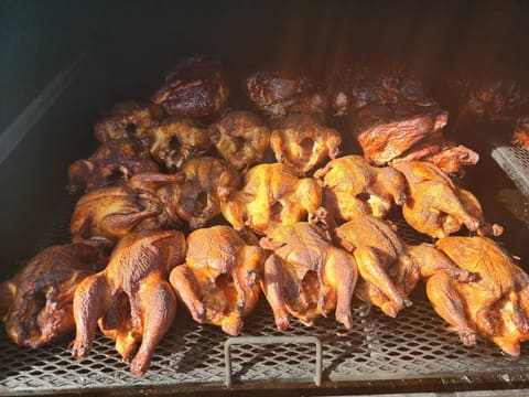 Roughly twenty whole chickens packed across the smoker grate, skin burnished deep gold and amber.